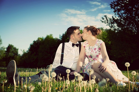 热恋的情侣在春公园草地上坐着要亲吻传统约会穿着衣服的女人和穿着领结的吊带男人浪漫情侣准备在草地上亲吻传统约会穿着服装的女人和穿紧图片