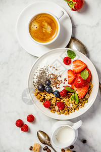 健康早餐咖啡和一碗自制麦片加酸奶和新鲜果子在白大理石背景上最顶端平地咖啡酸奶面粉和浆果背景图片
