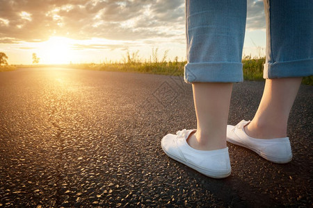 白色运动鞋上的妇女站在通往太阳的沥青路上新的开始旅行自由等概念旅行自由概念图片