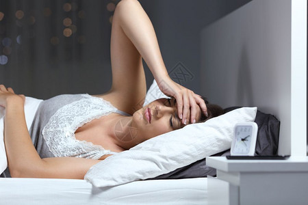 妇女头痛前额手痛晚上躺在家中的床图片