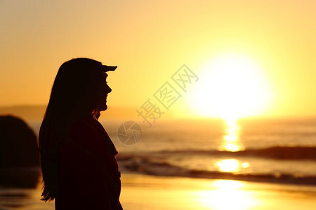 一个充满希望的女人侧面视线展望未来与双手在日落时的前额与日光和海在背景中图片