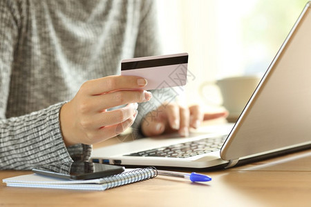 一名近身手贴妇女用信卡和家里一台式电脑上笔记本电脑在家中用信卡和一台笔记本电脑支付工资图片