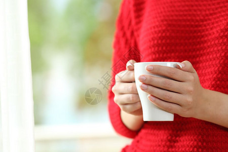 身着红色毛衣手握着咖啡杯站在窗外图片