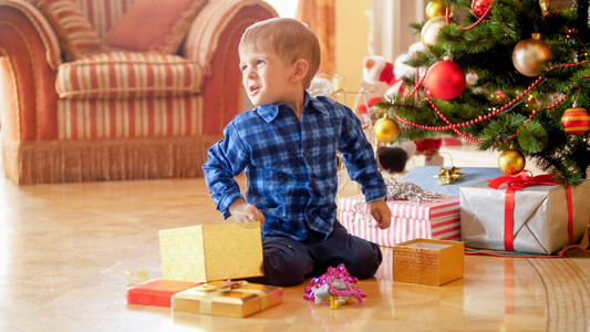 坐在地板上拿着圣诞礼物坐在地板上拿着圣诞礼物的愤怒男孩图片