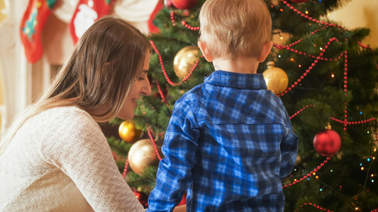 年轻母亲帮助其小儿子在客厅装饰圣诞树年轻母亲的肖像帮助其小儿子在客厅装饰圣诞树图片