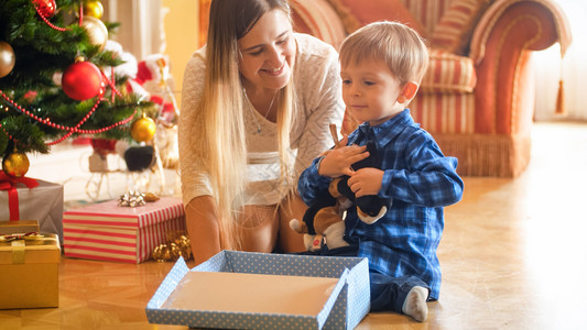 坐在圣诞树下面的快乐男孩肖像和开着礼物盒的图片