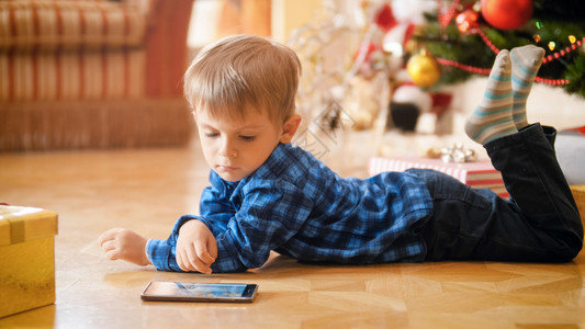 小男孩躺在圣诞树下智能手机上看视频小男孩躺在圣诞树下智能手机上看视频图片