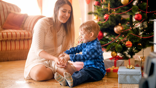3岁男孩与母亲一起坐在客厅圣诞树下图片