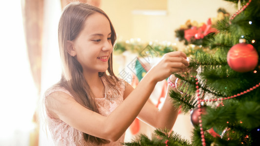 笑的少女在圣诞树上放多彩的和珠子肖像图片