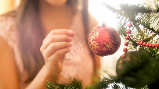 年轻女孩在圣诞树枝上贴红色的金闪亮剂照片图片
