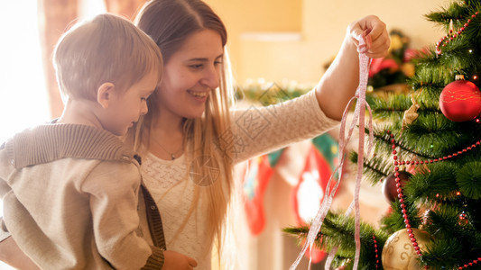 快乐的母亲肖像有小男孩装饰圣诞树配着彩色的丝带图片