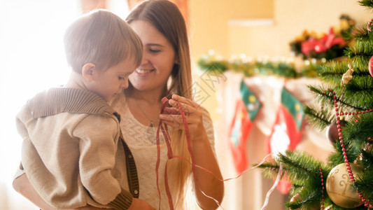美丽的母亲在客厅圣诞树旁边拥抱着小男孩美丽的微笑着年轻母亲在客厅的圣诞树旁边拥抱着小男孩图片