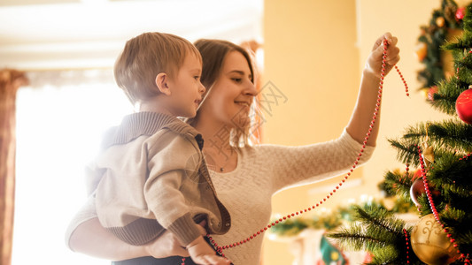 微笑的男孩肖像与母亲一起装饰圣诞树的模样与母亲一起装饰多彩珠子的模样微笑男孩和母亲一起装饰圣诞树的模样与母亲一起装饰多彩珠子的模图片