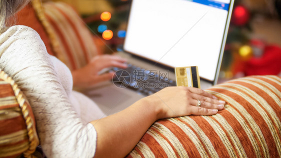 年轻女坐在圣诞树旁边的扶手椅上并在线商店订货图片