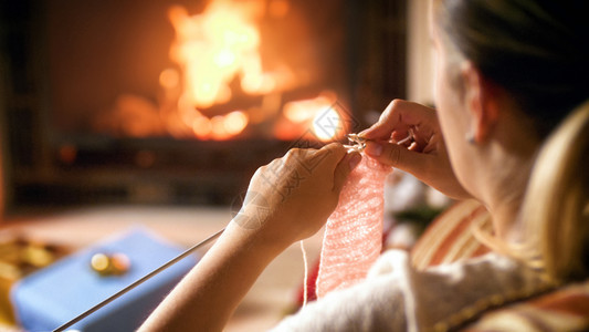 年轻女坐在壁炉和织羊毛跳跃器上年轻女坐在壁炉和编织羊毛跳器上图片