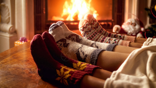 家庭穿着温暖的羊绒袜子躺在燃烧的壁炉旁沙发上家庭穿着温暖的针织袜子在燃烧的壁炉旁边沙发上图片