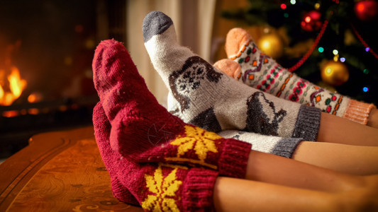 在圣诞树旁边的暖袜子和燃烧壁炉上紧贴着家庭脚和温暖的袜子照片紧贴着家庭脚的照片紧贴着圣诞树旁边的暖袜子和燃烧壁炉图片