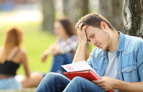 单身悲伤学生在公园的草地上检查一次考试失败图片