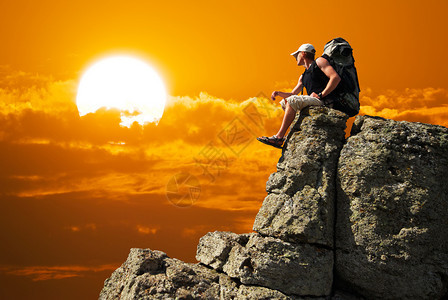 观光客坐在岩石上仰望边缘悬崖上的太阳图片