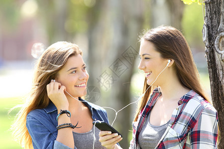 两个快乐的朋友分享在线音乐与耳花分享在公园户外图片