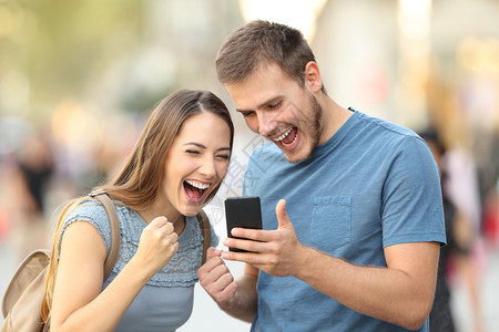 兴奋的一对夫妇在街上用智能电话在线接到好消息图片
