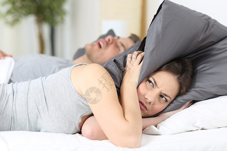 男人打呼噜而他的妻子却用枕头遮耳图片