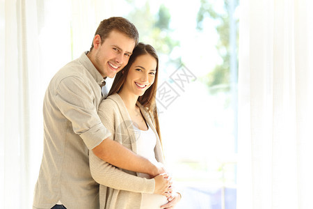 怀孕妇女和丈夫在家中看照相机的肖像图片