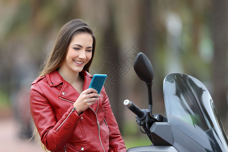 快乐的摩托车手检查智能机在她的摩托车上在街图片