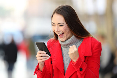 一个在街上冬季用智能手机阅读好消息的兴奋女性肖像图片