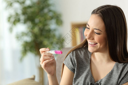 在家里起居室沙发上检查怀孕测试的快乐妇女图片