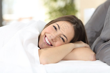一个快乐女人的肖像一个完美的白色笑容躺在舒适的床上看着温暖背景的相机图片
