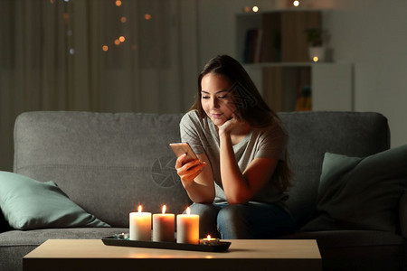 放松的女孩在晚上打电话家里客厅的沙发上坐着蜡烛灯图片