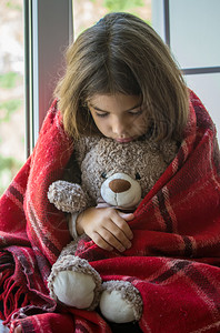 坐在窗台上的可怜小女孩躲在一个老的格子后面仔细地拥抱着她可爱的