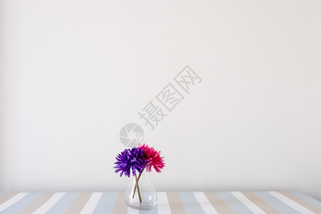 白墙背景上桌边花朵的玻璃瓶图片