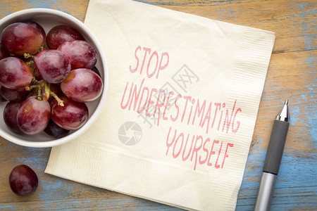 停止低估你自己鼓舞人心的笔迹在餐巾纸上与新鲜葡萄图片