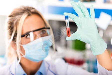 在科学化研究实验室使用红色液体样本物质探测器进行保护眼镜和面具检查试验管的年轻有吸引力女科学家图片