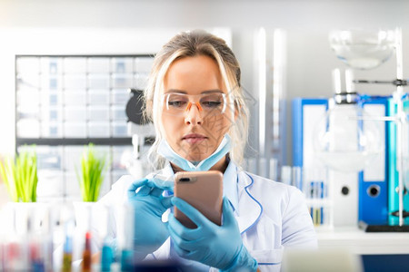 年轻有吸引力的女科学家在化实验室使用智能手机保护眼镜图片