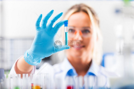 在科学化研究实验室使用红色液体样本物质探测器进行保护眼镜和手套检查试管的年轻有吸引力女科学家图片