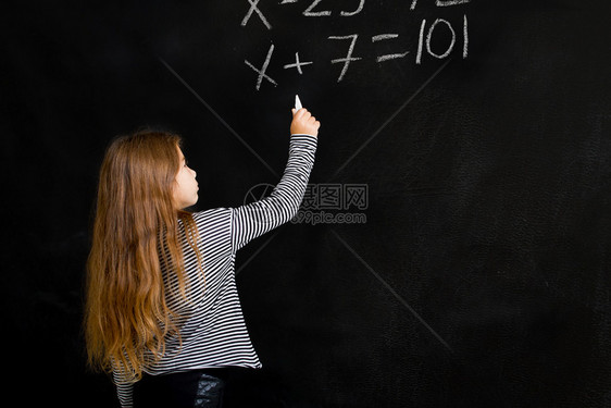 一个小女孩站在学校董事会旁边试图解决她数学上的一个困难任务图片