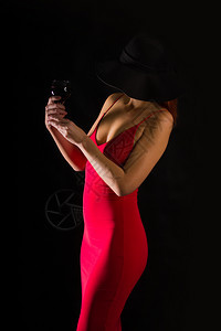 穿着亮红礼服的感女孩穿着黑色宽厚的帽子站在黑暗背景的酒杯上女孩帽子和酒图片