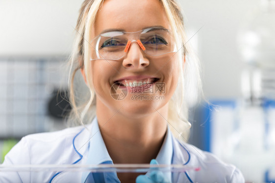 在科学化实验室里带着保护眼镜的快乐年轻有魅力微笑着女科学家肖像图片