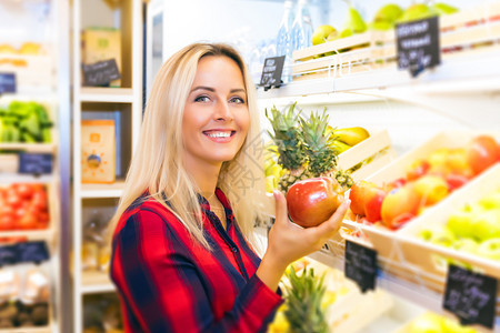 在食品店手里握着新鲜红苹果的年轻有魅力笑着容的年轻女士图片