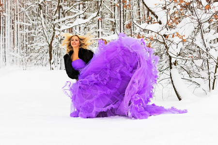 穿着长紫色裙子的金发年轻美女在雪的冬季森林或户外的木里图片