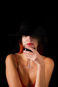穿着红发裙子的感女孩喝着酒杯来自黑暗背景的杯子图片
