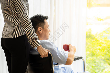 有红茶咖啡和坐轮椅亲属的老年人病正在透过窗户看图片