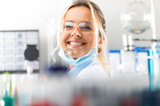 在科学化实验室里带着保护眼镜的快乐年轻有魅力微笑着女科学家肖像图片