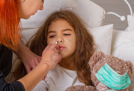 一个小女孩带着她最喜欢的泰迪熊身上戴着纱布绷带的小女孩躺在床上生病母亲在鼻子里滴药图片