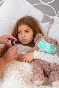 一个小姑娘带着最喜欢的泰迪熊被他们绑在纱布绷带上躺在床生病母亲在喝药图片