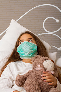 一个小女孩带着她最喜欢的玩具熊躺在床上生病脸贴着纱布绷带图片
