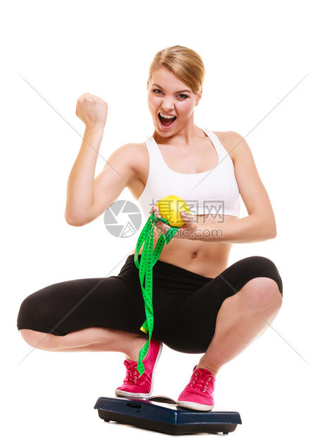 减肥快乐的成功年轻女孩快乐的成功年轻女孩与测量磁带体重称握着葡萄精紧她的拳头健康生活方式概念孤立于白种背景图片
